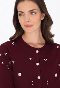 Burgundowa kardiganka prążkowana z perłowymi i rhinestonowymi zdobieniami, z okrągłym dekoltem i zapięciem na guziki.