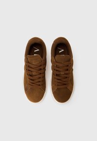 Brown suede sneakers with a textured surface and rounded shape, featuring laces, a white rubber sole, and minimalist branding on the insole.