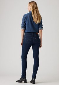 Tummansiniset skinny-farkut, joissa on korkea vyötärö, yhdistettynä rullatuilla hihoilla varustettuun farkkupaitaan. Suora pinta ja klassinen viiden taskun muotoilu.