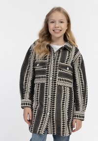 Musta ja kermainen kuvioitu takki nappikiinnityksellä, jossa on kaksi rintataskua ja pitkät hihat. Takissa on vaihtelevaa geometriaa ja tekstuureja.