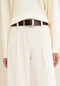 Cremfarbene, weit geschnittene Hosen, kombiniert mit einem hell gestreifen Pullover, gesichert durch einen schwarzen Ledergürtel mit einer silbernen Schnalle.