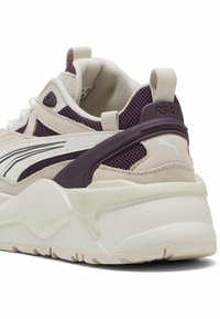 RS-X sneakers feature a blend of cream and deep purple materials, textured mesh, and a chunky white sole with prominent branding on the heel.