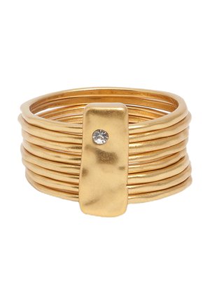 Anillo de múltiples bandas en tono dorado con una placa rectangular de oro que presenta una pequeña piedra preciosa transparente en el centro.