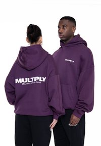 Fialové bavlnené mikiny s oversized strihom. Na prednej strane malá ikona a na zadnej strane veľký nápis "MULTIPLY" s detailmi klubu. Obsahuje klokaní vrecko.