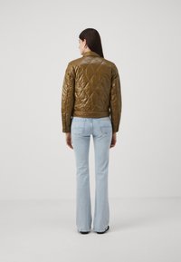 Giacca imbottita marrone con colletto alla coreana e maniche lunghe, abbinata a jeans a zampa d'elefante di un delicato blu. La giacca presenta motivi a rombi.