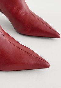 Rote Leder-Pumps mit spitz zulaufender Spitze, glatter Textur und sichtbaren Nähten, ausgestattet mit einem schlanken, hohen Absatz.