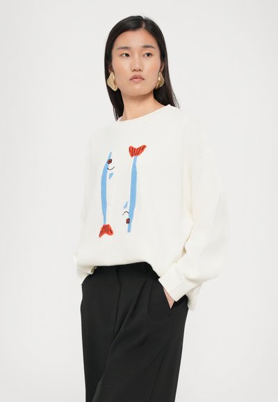 Witte trui met blauwe en rode visborduring aan de voorkant. Zacht gebreid materiaal, relaxed fit, geribbelde manchetten en zoom. Gemaakt in combinatie met zwarte broek.