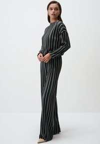 Lang, gestreepte jurk in donkergroen, met verticale lijnen in beige, roze en teal. Slanke pasvorm met lange mouwen en een hoge halslijn.