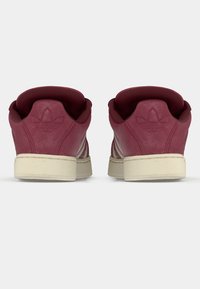 Ζευγάρι από μπορντό σουέτ αθλητικά παπούτσια με μπεζ σόλες, εμφανιζόμενα από πίσω, με ανάγλυφο λογότυπο στη φτέρνα και επενδεδυμένους περιμετρικά αστραγάλους.
