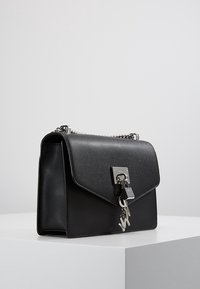 Borsa a tracolla in pelle nera con design strutturato, accessori in argento, un dettaglio con lucchetto e tracolla a catena. Texture liscia con una finitura opaca.