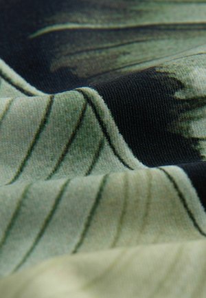 Kangastikand, millel on kihiline kujundus roheliste ja mustade mustritega. Kangas on ribakujuline ja sellel on diagonaalsed triibud ning pehmed voldid.