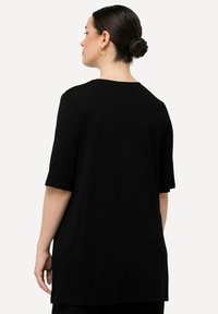 Top in maglia nera con maniche corte, scollatura rotonda e taglio dritto. Texture liscia e vestibilità comoda. Nessun motivo o dettaglio visibile.