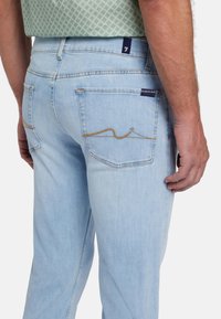 Jeans in denim azzurro chiaro con vestibilità dritta, dotati di tasche posteriori con cuciture gialle e un'etichetta in tessuto sulla vita.