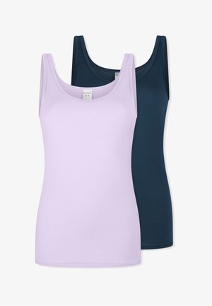 Frau trägt ein eng anliegendes hellviolettes Tanktop und passende Unterwäsche, steht vor einem einfarbigen hellen Hintergrund.