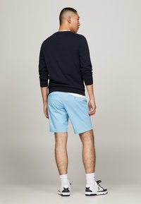Maglietta a maniche lunghe blu navy abbinata a pantaloni corti azzurri, con fascia in vita piatta e tasche posteriori, indossata con calze atletiche bianche e scarpe nere.