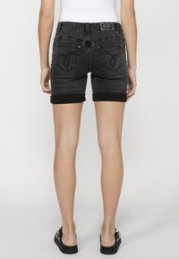 Črne denimske kratke hlače s zavihanimi robovi, ki imajo dve zadnji žepi in okrasno šivanje. Material je teksturiran z izbledelim videzom.