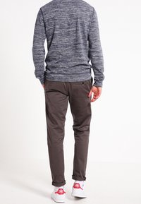 Maglione blu a trama, pantaloni grigi a gamba affusolata, sneakers bianche con dettagli rossi, che mostrano un look casual e rilassato visto da dietro.