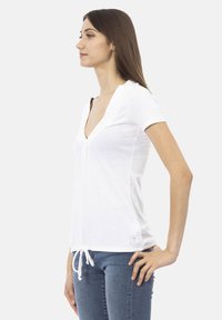 T-shirt bianco a maniche corte con scollatura a V, dotato di un dettaglio arricciato sul davanti e cordoncino regolabile all'orlo. Materiale in cotone liscio.