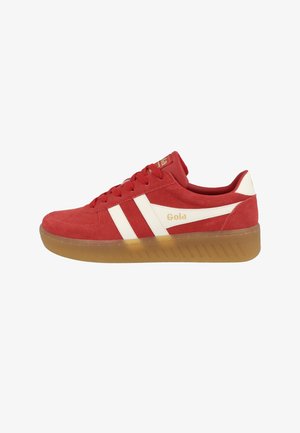 Zapatillas de gamuza roja con rayas blancas, suela de goma texturizada y logo dorado en la lengua. Diseño de corte bajo con cuello acolchado para mayor comodidad.