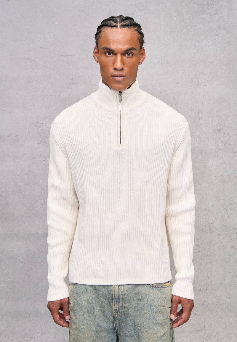 Maglione bianco a coste con colletto alto e metà zip, tessuto testurizzato, maniche lunghe e vestibilità comoda, abbinato a denim chiaro.