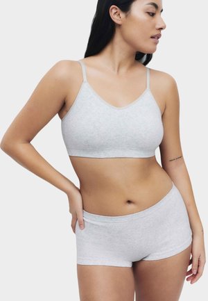 Woman wearing light gray seamless bralette and matching boyshort underwear, standing with hand on hip, looking to the side.