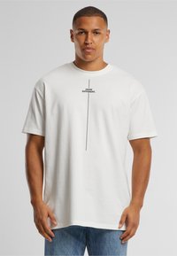 Camiseta de algodón blanca con mangas cortas, que presenta una impresión vertical en negro con el texto "PENSAR DIFERENTE" en el centro. Diseño de corte relajado.