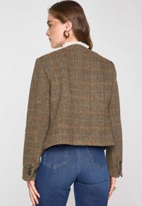 Bruine cropped jas met een visgraatpatroon en knoopmanchetten, voorzien van een gestructureerde afwerking en een kanten kraag die boven de halslijn uitsteekt.