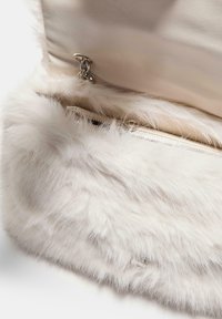 Primo piano di una borsa in pelliccia sintetica bianca con un interno in pelle beige e una tracolla in catena argentata.