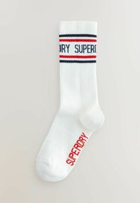 Witte geribde sokken met blauwe en rode strepen aan de bovenkant en "SUPERDRY" in het rood gedrukt op de zijkant. Standaard crewlengte.