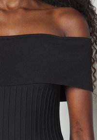 Top nero a coste scollato spalle con silhouette aderente, caratterizzato da motivi a coste orizzontali e verticali, texture morbida e senza hardware visibile.
