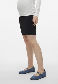 Pantofi din denim albastru cu vârful rotund și curea la gleznă, având un accent circular mic. Purtați cu o fustă neagră și un top alb cu mâneci lungi.