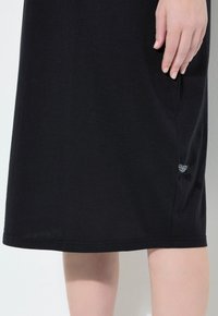 Vestito in cotone nero con taglio dritto, un logo discreto vicino all'orlo e una texture liscia con dettagli di cucitura minimali.