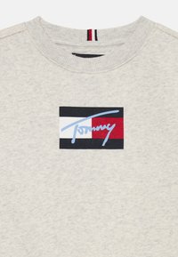 Sweatshirt gris à col ras du cou avec un patch logo coloré en bleu, rouge, blanc et noir, et une finition en tissu texturé.