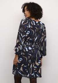 Fließendes, plissiertes Kleid in blau, schwarz und beigen Mustern. Mit einem elastischen Taillenbund und puffärmeligen, runden Ausschnitt.