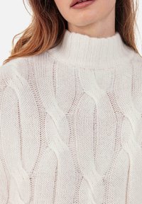 Pullover mit Zopfmuster aus weicher weißer Wolle; verfügt über einen hohen, gerippten Kragen und strukturierte Muster in einem lockeren, grob gestrickten Design.