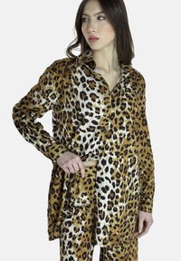 Camisa de estampado de leopardo marrón y blanco, hecha de una tela suave; cuenta con cuello y botones, con mangas largas y un corte holgado.