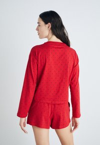 Röd pyjamasuppsättning med långärmad topp och shorts, med små blå hjärtmönster. Mjuk tyg, avslappnad passform och lätt design.