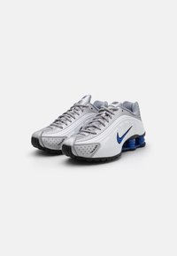 Weiße und graue Sportschuhe mit einem glatten Synthetik-Obermaterial, durchbrochenen Details, blauen Akzenten im Logo und einer markanten, gepolsterten Sohle.