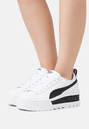 Białe sneakersy na platformie wykonane z syntetycznej skóry, z czarnymi paskami akcentującymi, z okrągłymi sznurowadłami i textured czarną panelą na pięcie.