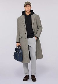 Szary wełniany płaszcz o dopasowanym kroju, czarna bluza z kapturem, jasnoszare spodnie, czarne buty i niebieska torba. Stanowi uzupełnienie codziennego, warstwowego stylu.