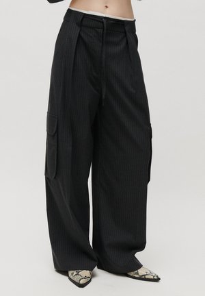 Black wide-leg pinstripe pants with side cargo pockets worn with snakeskin pointed-toe shoes on a white background.