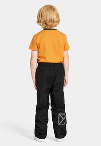 Oranssi lyhythihainen paita mustilla yksityiskohdilla, yhdistettynä mustiin housuihin, joissa on heijastava logo ja joustava vyötärö, viimeistelty valkoisilla kengillä.