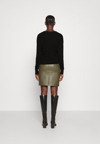 Svart stickad tröja, olivgrön läderkjol och knähöga svarta klackstövlar. Tröjan har en diskret design runt halsringningen.