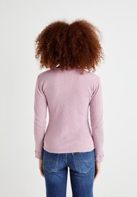 Haut à manches longues en rose clair, à côtes, avec un col rond et une coupe ajustée. Associé à un jean bleu moyen.