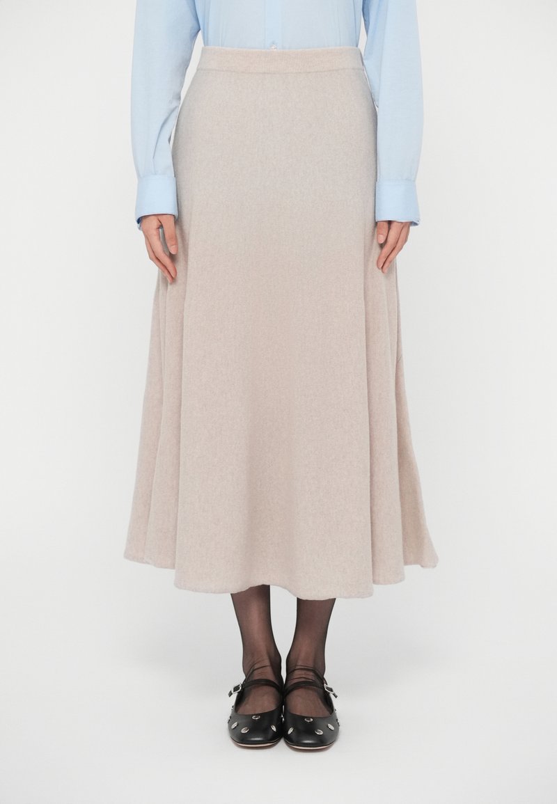 Beige, polvipituinen hame, valmistettu pehmeästä kankaasta, jossa liehuva malli. Yhdistetty vaaleansiniseen paitaan ja mustiin kenkiin, joissa hopeanväriset niitit.