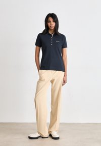 Ναυτικό πόλο μπλούζα με κοντά μανίκια και πλακάζ τριών κουμπιών, διαθέτοντας φάσα λευκού χρώματος στον γιακά. Συνδυάζεται με μπεζ παντελόνι με φαρδιά γραμμή και λευκά μοκασίνια.