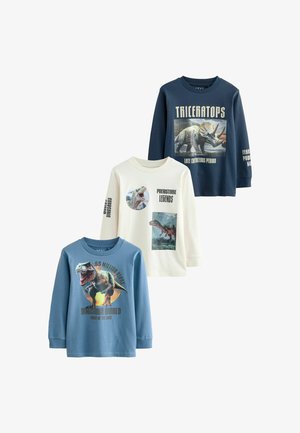 Tres camisetas de manga larga: una en azul marino con un gráfico de triceratops, una crema con una ilustración de T. rex y una celeste claro con estampado de dinosaurios y texto. Tejido de algodón.