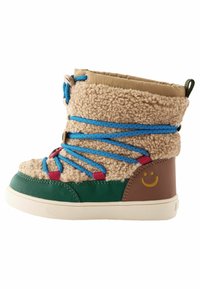 Botte en polaire beige avec des lacets bleus et roses, base en tissu vert, talon marron avec un visage souriant, et un col rembourré beige.