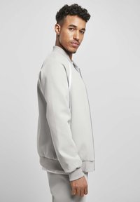 Hele hall bomber jacket, mis on valmistatud pehmest kangast, litsimisega ning ribidega mansettidega, valgete aktsentidega varrukate ääres.
