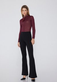 Burgundská košile s dlouhým rukávem zkombinovaná s černými kalhotami s vysokým pasem a rozšířenými nohavicemi. Outfit doplňuje vzorovaný šátek na krk a černé podpatky. Hladká textura.
